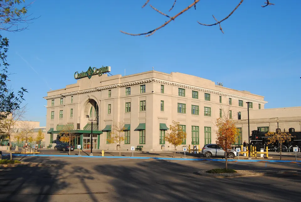 Casino Regina in the former Union Station, a pale stone building with an arched entrance, green awnings and a steam locomotive on display beside it